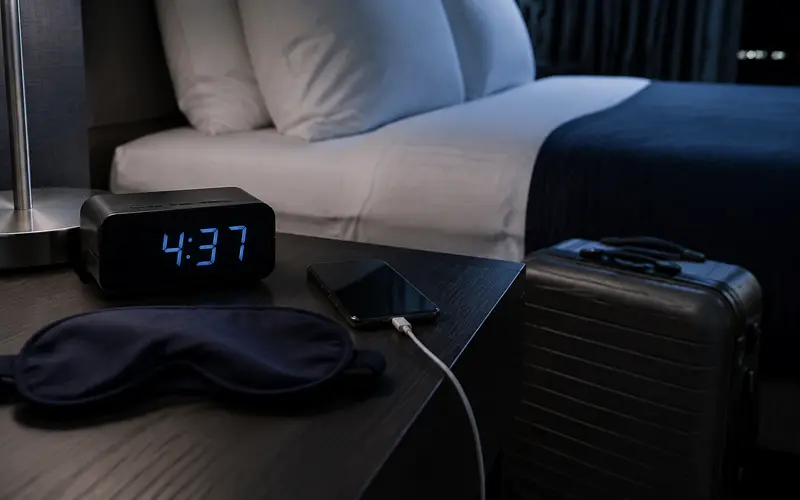 Alarm clock and sleep mask beside a hotel bed before an early flight