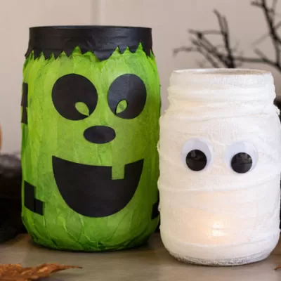 Frankenstein and mummy mason jar lanterns glowing beside pumpkins and Halloween decorations
