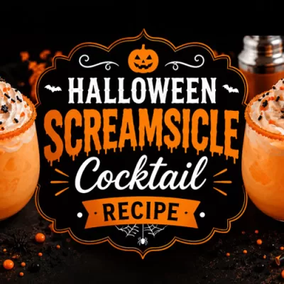Halloween Screamsicle cocktail topped with whipped cream and black and orange sprinkles surrounded by pumpkins, spooky decor, and glowing candlelight.