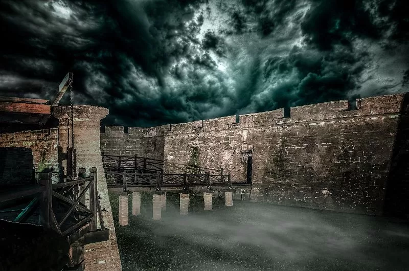 Dark and eerie view of Castillo de San Marcos in St. Augustine with storm clouds overhead and mist surrounding the historic stone fort at night.