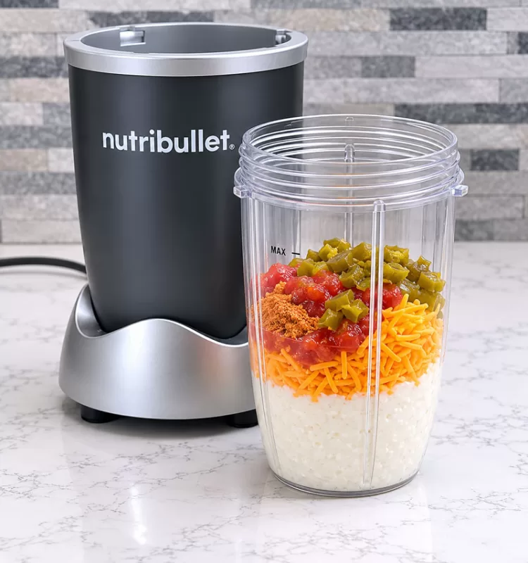 Nutribullet blender with cottage cheese queso ingredients layered in a blender cup including cheddar cheese, salsa, taco seasoning, and jalapeños.