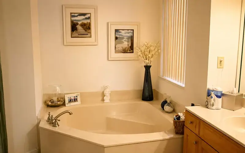 Bathroom with soft white lighting featuring a corner soaking tub and warm cozy atmosphere