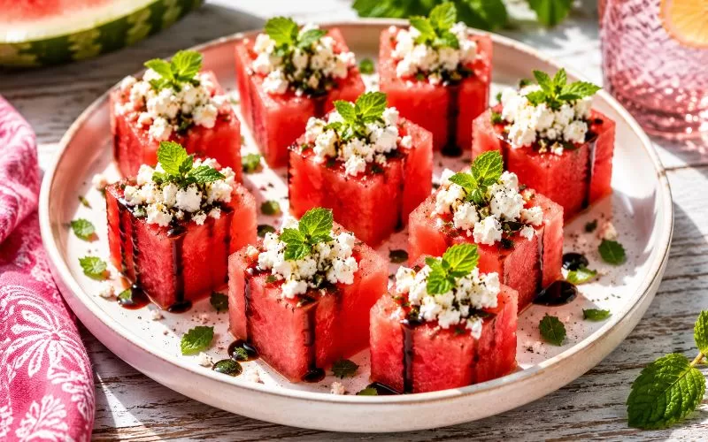 Watermelon feta cups topped with fresh mint and balsamic glaze on a white plate for a healthy summer snack.
