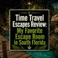 Jurassic-themed escape room image with a wooden bridge over blue fake water, jungle walls, tropical plants, a dinosaur, and centered text reading Jurassic Adventure Complete Review.