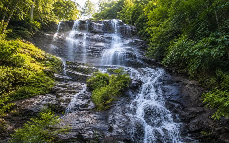 Multi-tiered waterfall flowing over dark rock ledges surrounded by dense green forest