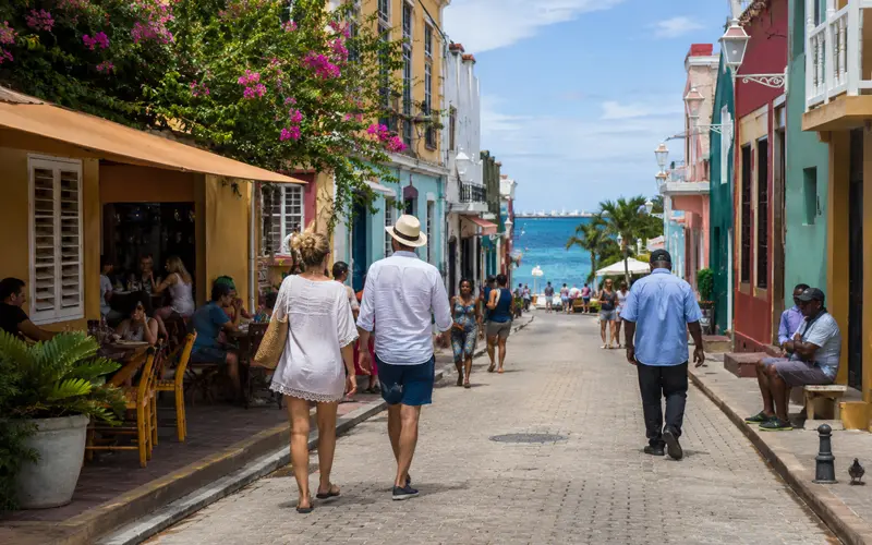 Travelers exploring a colorful Caribbean coastal town near the water.