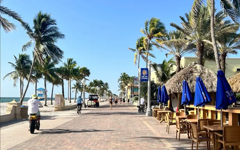 Hollywood Beach Broadwalk lined with palm trees, beachfront restaurants, cyclists, and people walking near the ocean